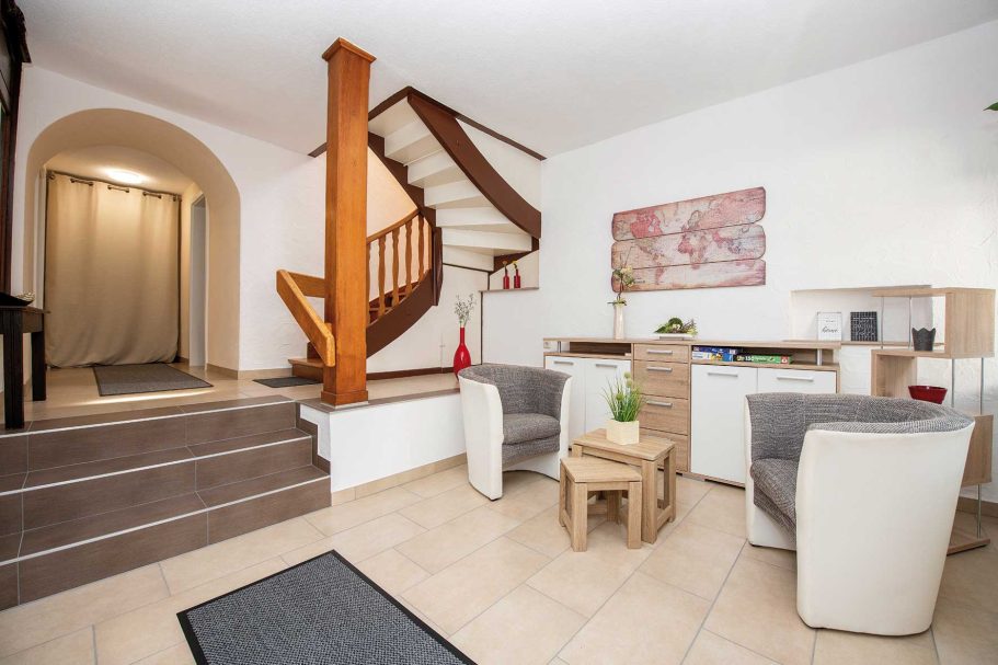 Heller Eingangsbereich mit Treppe, Tischen und Stühlen. Holz- und helle Farbtöne dominieren.