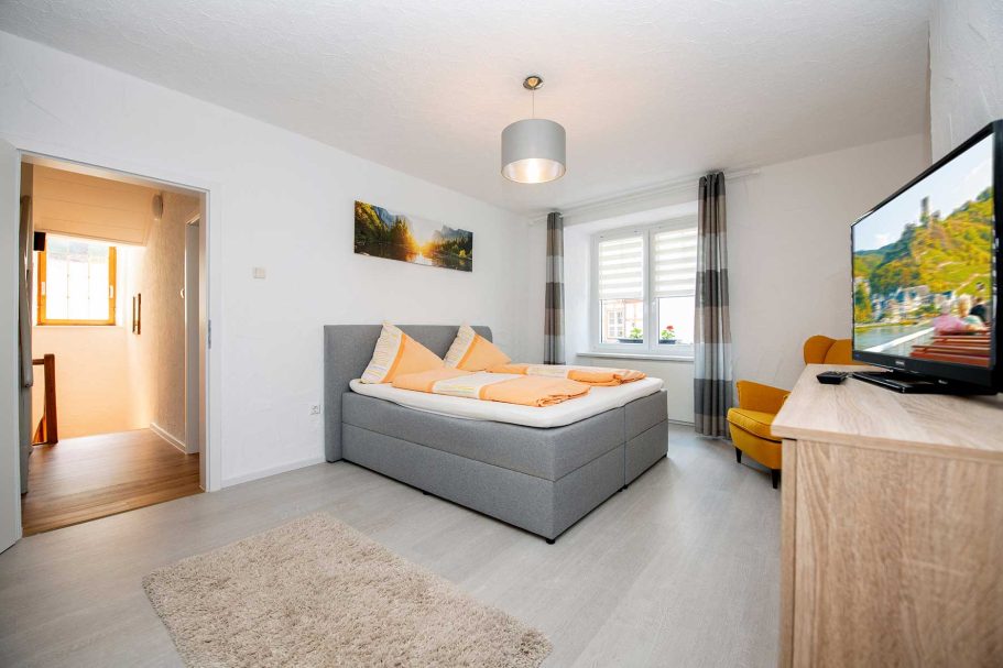 Helles Schlafzimmer mit Doppelbett, Fernseher und gemütlichem Sessel.