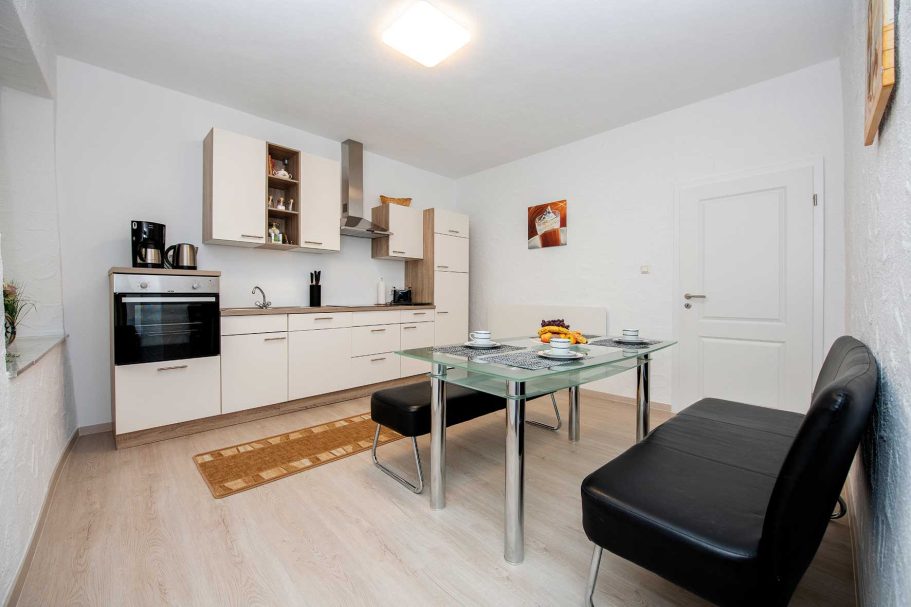 Helle moderne Küche mit einem Esstisch, schwarzen Stühlen und modernen Geräten.